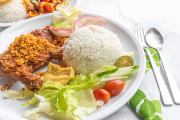 Ayam Penyet is Indonesian, East Javanese cuisine - consisting of fried chicken that is smashed with the pestle against mortar to make it softer, served with sambal chilli. Food on table concept.