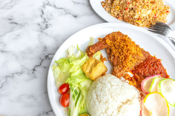 Ayam Penyet is Indonesian, East Javanese cuisine - consisting of fried chicken that is smashed with the pestle against mortar to make it softer, served with sambal chilli. Food on table concept.