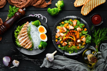 Dishes of chicken meat and vegetables in a black plate on a black background. Buddha bowl. Top view. Free space for your text.