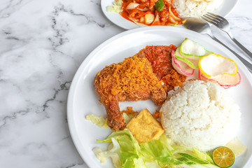 Ayam Penyet is Indonesian, East Javanese cuisine - consisting of fried chicken that is smashed with the pestle against mortar to make it softer, served with sambal chilli. Food on table concept.