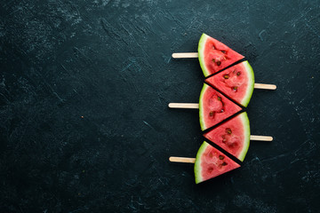 Watermelon popsicle on black background. Watermelon slices on sticks. Top view. Free copy space.