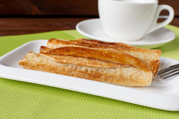 Fried pancakes roll into a tube on a white plate with tea. Green napkin.