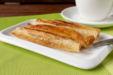 Fried pancakes roll into a tube on a white plate with tea. Green napkin.