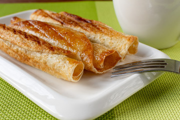Fried pancakes roll into a tube on a white plate with tea. Green napkin.