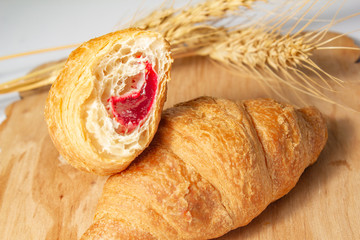 bitten croissants with strawberry jam with dry wheat on a wooden board on a white background