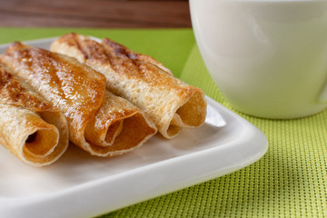 Fried pancakes roll into a tube on a white plate with tea. Green napkin.