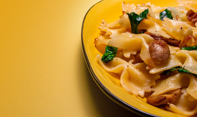 butterfly pasta with fried mushrooms, green spinach on a yellow plate on an orange background. copy space