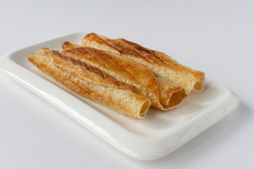 Fried pancakes roll into a tube on a white plate with a white background.