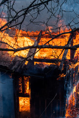 Charred in flame house at night. Fire everywhere and smoke in a residential area at night. Dangerous fire. Whole house and yard on fire. A fire destroys a charred burnt house.