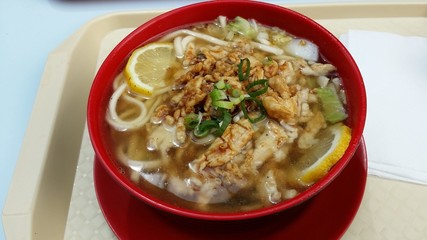 Ramen asian soup with lemon slices and chicken meat in a red bowl and on a white plastic plate. It has slices onion as a topping.