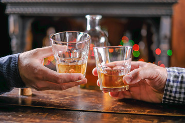 two hands raise glasses with whiskey in a bar on a wooden table