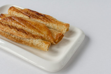 Fried pancakes roll into a tube on a white plate with a white background.