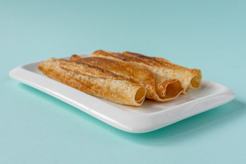 Fried pancakes roll into a tube on a white plate with a blue background.