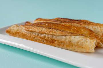 Fried pancakes roll into a tube on a white plate with a blue background.
