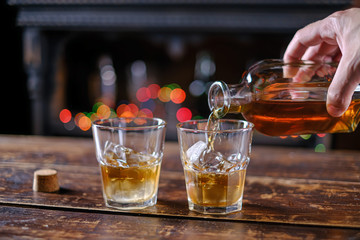 The waiter pours whiskey in a bar on a wooden table in an old-fashioned glass