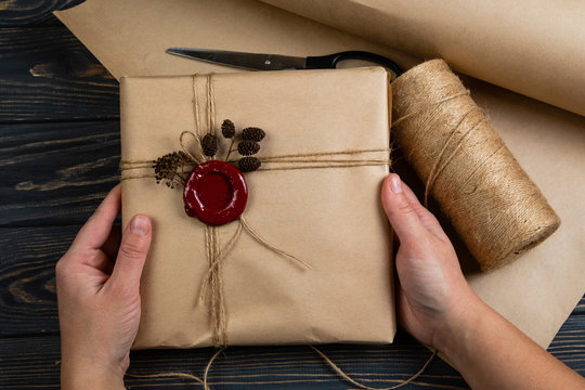 Process of package gift wrapped in craft paper, tied with string and glued wax seal on wooden black background