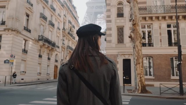 Camera follows happy beautiful woman smiling, walking towards Eiffel Tower along warm autumn Paris street slow motion.