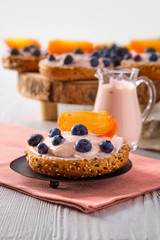 Closeup view of sweet buns with yogurt, blueberry and slice of persimmon on white wooden table