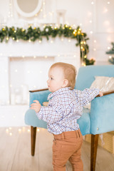 Cute little boy by the Christmas tree and fireplace decorated with garlands and gifts. Christmas mood