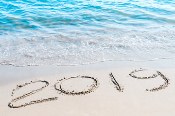 End of  2019 handwritten on the sandy beach with ocean wave washing away with water.. Happy new year 2020 concept.