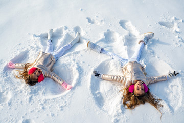 Two Girls on a snow angel shows. Children playing and making a snow angel in the snow. Top view.