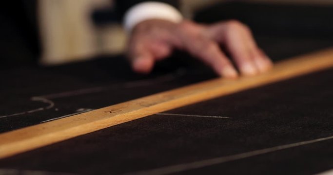 Close up footage of a tailor drawing lines on fabric and making some alterations arround the cut with his chalk