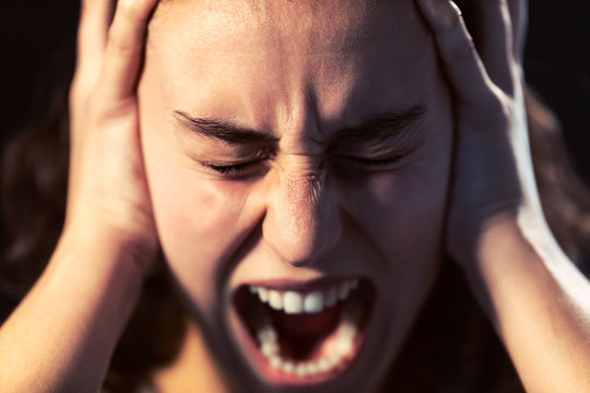 A young woman close-up screaming on black background. Mental illness concept.