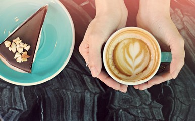 Woman's hands holding a cup of hot cappuccino coffee, giving and kindness concept.
