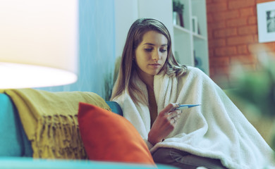 Young woman with cold and flu measuring her temperature