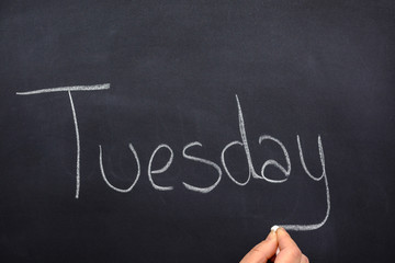 Woman's hand writing the day of the week on a blackboard with white chalk, tuesday