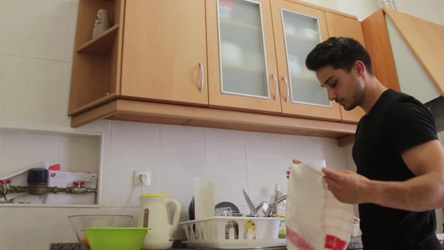 Young Man in Black Shirt Putting Clean Dishes Away in Cabinets