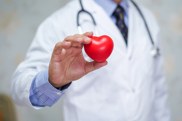 Doctor holding red heart in his hand in nursing hospital ward : healthy strong medical concept .