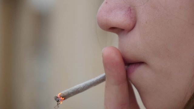 Close-up of a young girl's face as she is smoking a hand rolled cigarette or joint with copy space.