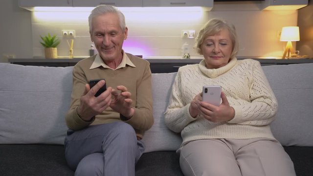 Happy old couple watching funny video on smartphone together, modern gadget