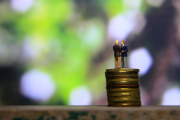 Simple Illustration Photo Successfull Bussiness Transaction, Two Man Handshaking at golden indonesia 500 Rupiah Coin, Green Forest as a background