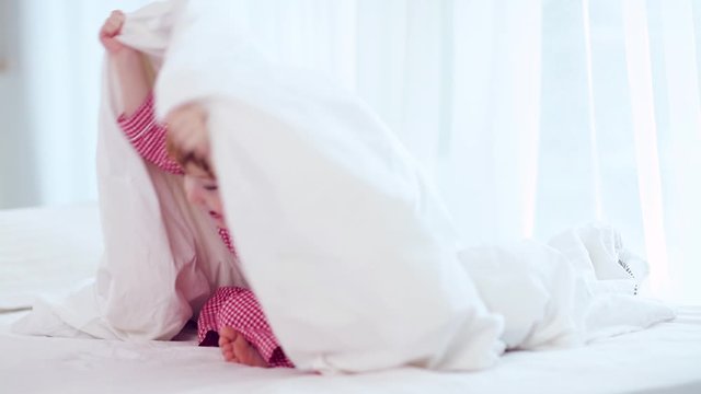 cute happy little boy, kid playing peekaboo, hiding under the blanket on the bed