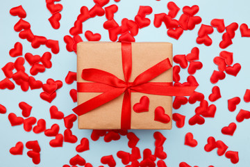 Present with red bow on blue background with heart confetti. Flat lay style. Valentine day concept