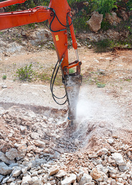 Hydraulic hammer works in a quarry against the background of huge stones