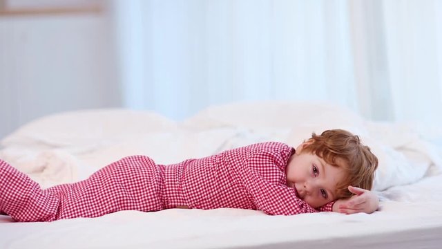 cute kid, boy in pajamas laying down on the bed in bedroom