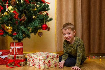 Obraz na płótnie Canvas Happy child boy with gift box near decorated fir tree. Merry Christmas celebration at home. Little smiling kid playing, having fun with present box. New Year family holidays.