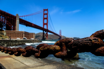 Naklejka premium USA San Francisco June 2018: Photo of the attractions of the Golden Gate Bridge near the water with waves, stones and chain
