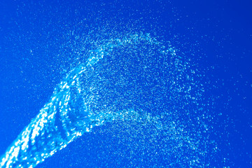 Abstract background. Blurry spray of water jet against a blue sky. Water glistens in the sun. Motion blur. Selective shallow focus. - obrazy, fototapety, plakaty