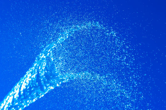 Abstract background. Blurry spray of water jet against a blue sky. Water glistens in the sun. Motion blur. Selective shallow focus.