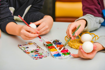 Fototapeta na wymiar Children paint eggs for Easter, a boy and a girl paint eggs with watercolors with a small brush.