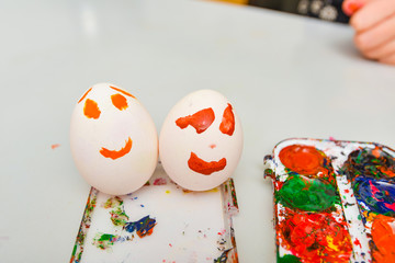 Two eggs with a painted face lie next to watercolors after art.