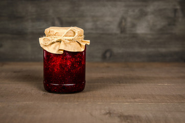 Jar with jam of berries wrapped in wrapping paper, on wooden background