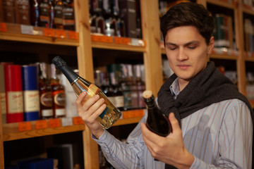 Low angle shot of a handsome young elegant man choosing wine to buy at the supermarket