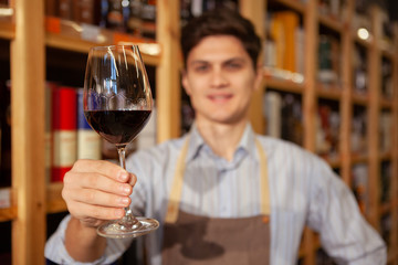Selective focus on a red wine glass in the hand of cheerful sommelier. Winemaker working at his shop