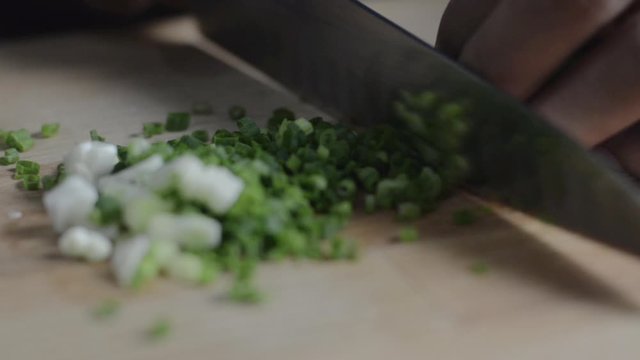 Close up chopping green onion with a knife on a wooden chopping board.
