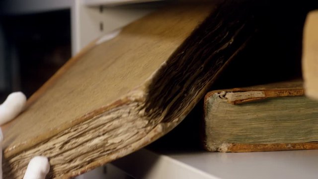 Expert takes an old book from the shelf. Stock footage. An ancient relic taken by gloved hands